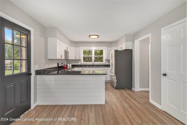 kitchen with appliances with stainless steel finishes, white cabinets, kitchen peninsula, light hardwood / wood-style flooring, and sink