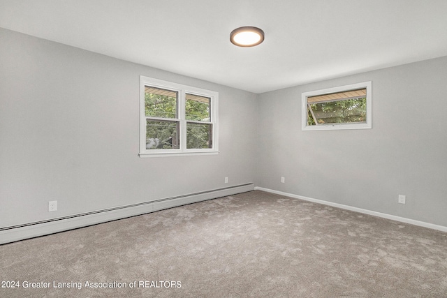 carpeted spare room featuring a baseboard heating unit and a wealth of natural light