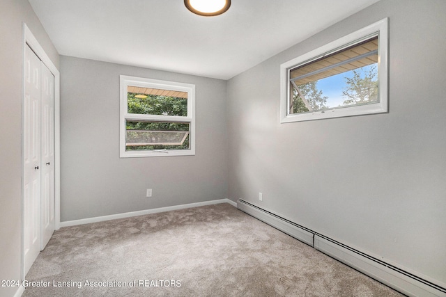 unfurnished bedroom with light carpet, a closet, and a baseboard heating unit