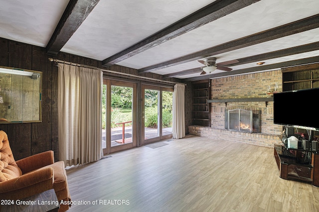 living room featuring ceiling fan, beam ceiling, a brick fireplace, wooden walls, and light hardwood / wood-style flooring