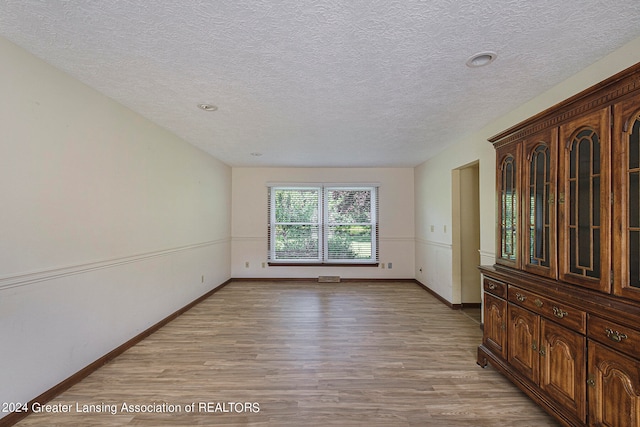 spare room with light wood-type flooring and a textured ceiling