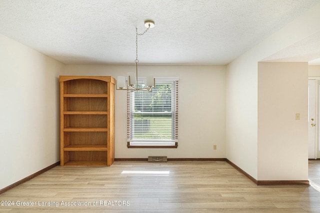 empty room with a notable chandelier, light hardwood / wood-style flooring, and a textured ceiling