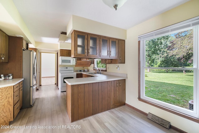 kitchen with light hardwood / wood-style flooring, white appliances, kitchen peninsula, and plenty of natural light