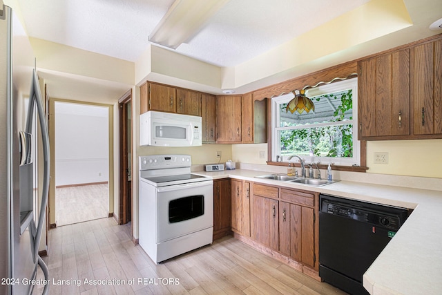 kitchen with light wood-type flooring, a textured ceiling, white appliances, and sink