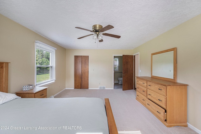 bedroom with a textured ceiling, light carpet, ensuite bath, and ceiling fan