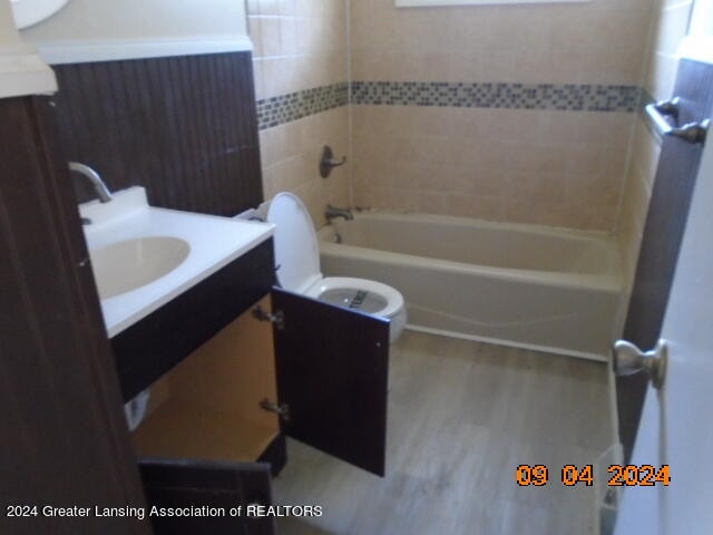 full bathroom with wood-type flooring, tiled shower / bath, vanity, and toilet