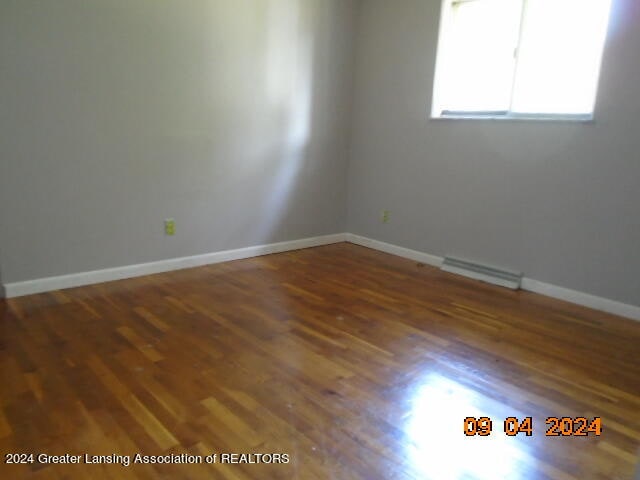 empty room featuring baseboard heating and hardwood / wood-style flooring