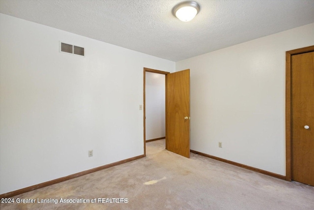 spare room featuring a textured ceiling and light colored carpet