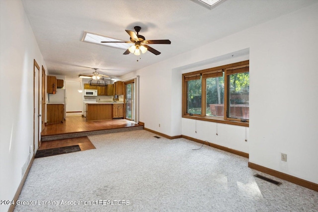 unfurnished living room with ceiling fan, a skylight, light carpet, and a textured ceiling