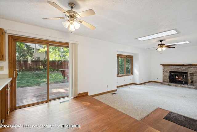 unfurnished living room featuring light wood-type flooring, ceiling fan, a fireplace, and a textured ceiling