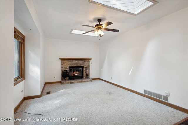 unfurnished living room featuring a textured ceiling, light colored carpet, a fireplace, a skylight, and ceiling fan