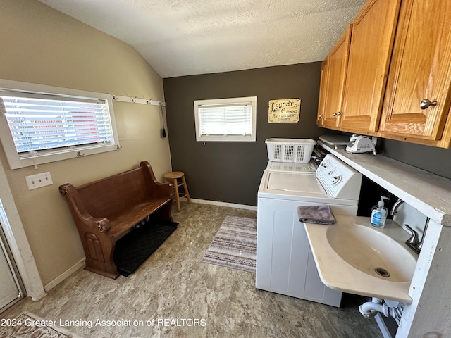 clothes washing area with a textured ceiling, cabinets, washing machine and dryer, and a wealth of natural light