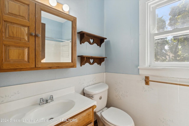 bathroom with a wealth of natural light, vanity, toilet, and tile walls