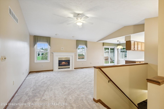 unfurnished living room with a premium fireplace, a healthy amount of sunlight, vaulted ceiling, and light colored carpet