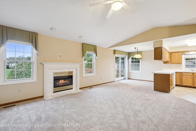 unfurnished living room with vaulted ceiling, a tiled fireplace, ceiling fan, and light colored carpet