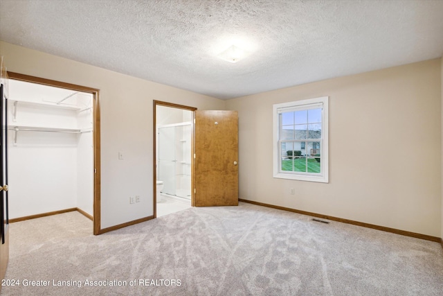 unfurnished bedroom featuring a closet, a textured ceiling, a walk in closet, ensuite bathroom, and light colored carpet