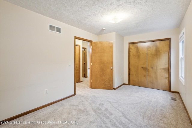 unfurnished bedroom with light colored carpet, a textured ceiling, and a closet