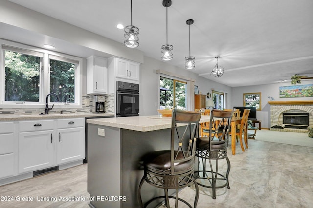 kitchen featuring pendant lighting, a center island, sink, a brick fireplace, and white cabinetry