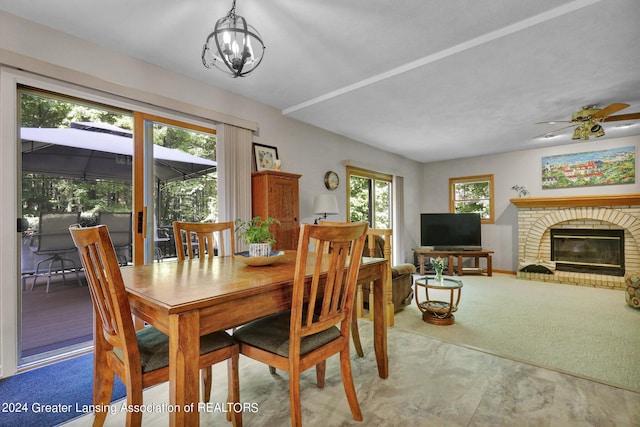 dining space with ceiling fan with notable chandelier, carpet floors, and a brick fireplace