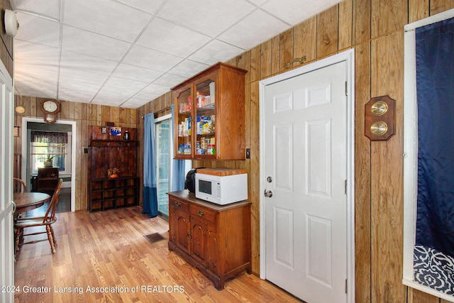 318 S Shiawassee St, Corunna, MI 48817 - kitchen with white microwave, wooden walls, glass insert cabinets, brown cabinets, and light wood finished floors