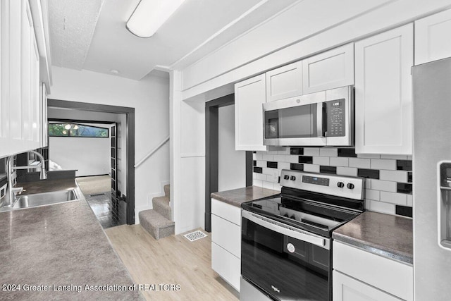 kitchen with white cabinets, sink, light wood-type flooring, tasteful backsplash, and stainless steel appliances