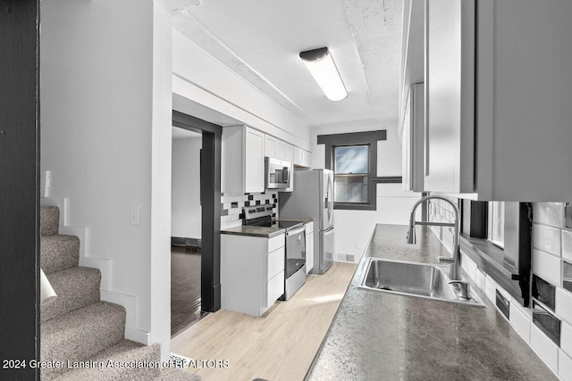 kitchen with white cabinetry, sink, stainless steel appliances, backsplash, and light hardwood / wood-style floors