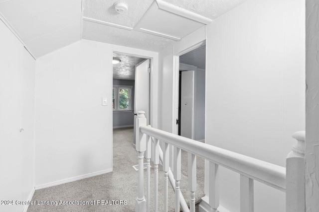 hall featuring a textured ceiling, light carpet, and lofted ceiling