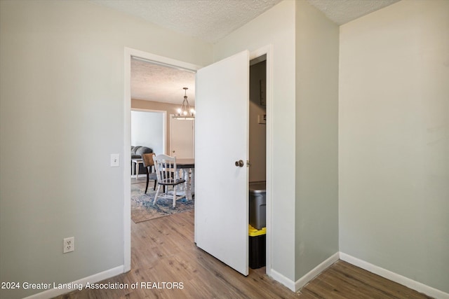 corridor featuring wood-type flooring, a textured ceiling, and a notable chandelier