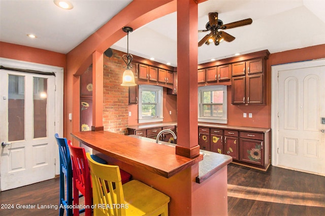 kitchen featuring kitchen peninsula, dark hardwood / wood-style flooring, ceiling fan, a kitchen breakfast bar, and pendant lighting