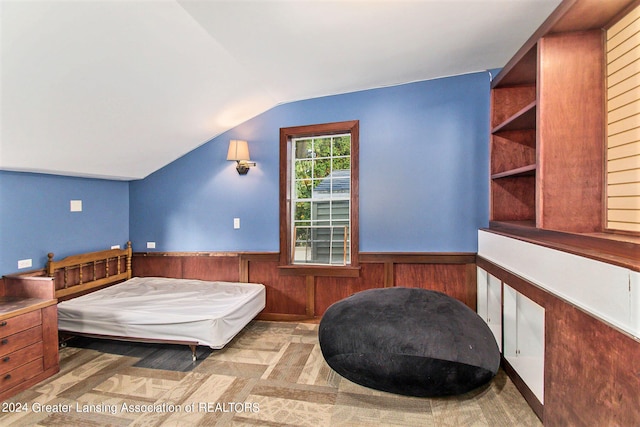 bedroom featuring lofted ceiling and wooden walls