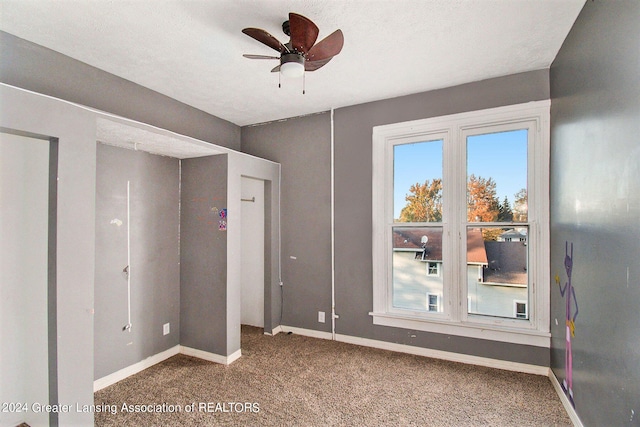 unfurnished bedroom with ceiling fan, a textured ceiling, and dark carpet