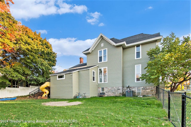 back of property featuring a yard, central AC, and a playground