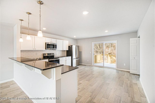 kitchen with hanging light fixtures, stainless steel appliances, white cabinets, kitchen peninsula, and light wood-type flooring