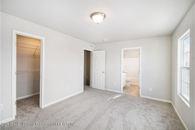 unfurnished bedroom featuring a walk in closet, connected bathroom, a closet, and light carpet