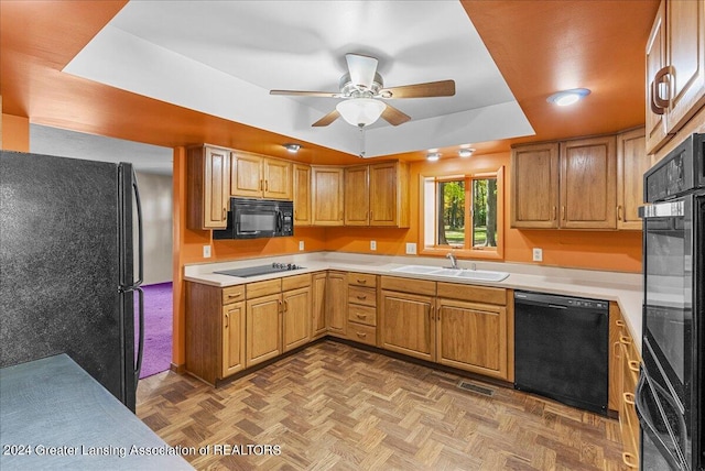 kitchen with ceiling fan, a raised ceiling, black appliances, sink, and light parquet floors