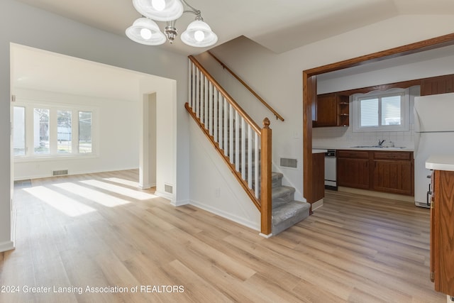 stairway with sink, an inviting chandelier, vaulted ceiling, and hardwood / wood-style flooring