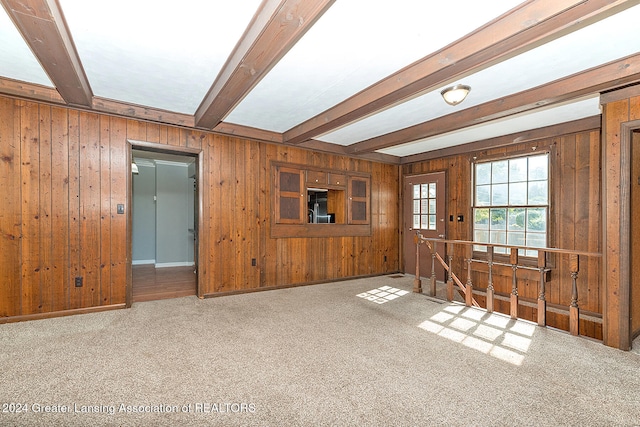 unfurnished living room with beam ceiling, wood walls, and carpet