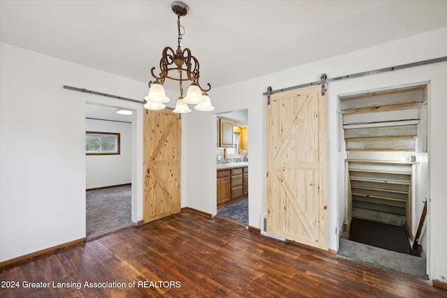 unfurnished dining area featuring an inviting chandelier, a barn door, and dark hardwood / wood-style floors