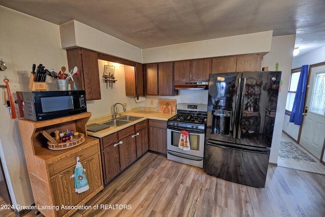 kitchen with light wood-type flooring, black appliances, under cabinet range hood, light countertops, and a sink