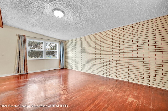 spare room with hardwood / wood-style flooring, a textured ceiling, brick wall, and vaulted ceiling