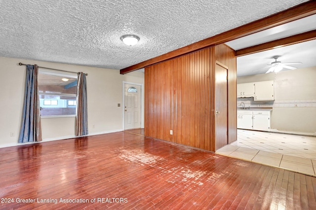 empty room featuring a textured ceiling, wood walls, beamed ceiling, ceiling fan, and light hardwood / wood-style flooring