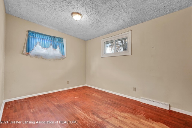 spare room featuring hardwood / wood-style floors, a baseboard radiator, and a textured ceiling