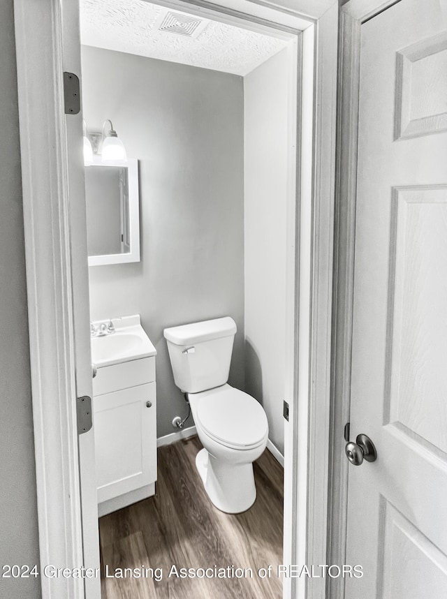 bathroom with a textured ceiling, hardwood / wood-style floors, vanity, and toilet