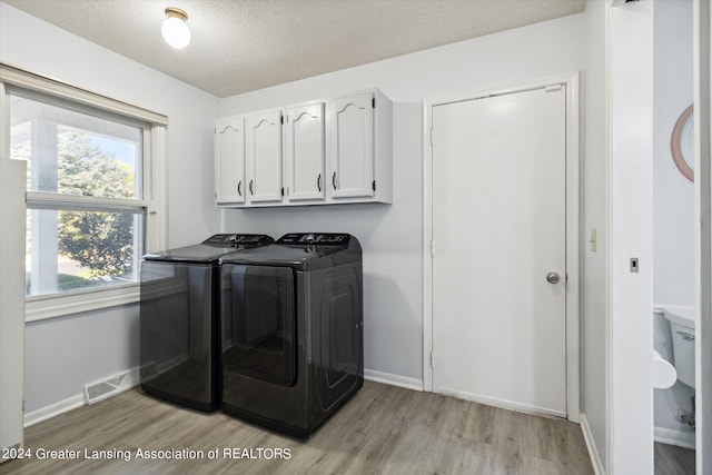 clothes washing area with cabinets, light hardwood / wood-style flooring, a textured ceiling, and washer and clothes dryer