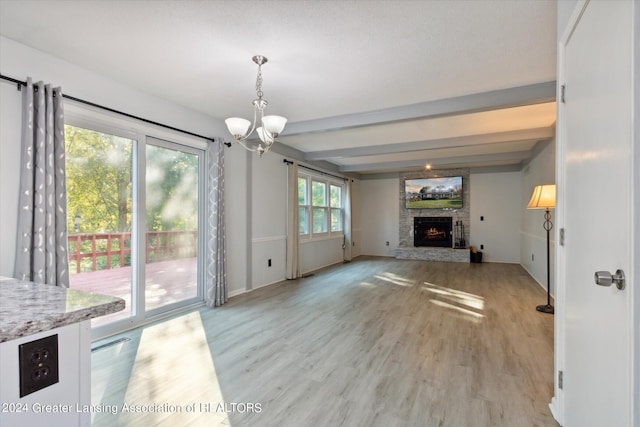 unfurnished living room with an inviting chandelier, beamed ceiling, a fireplace, and light wood-type flooring