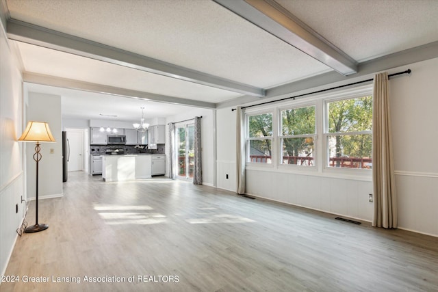 unfurnished living room with an inviting chandelier, beamed ceiling, light hardwood / wood-style flooring, and a textured ceiling