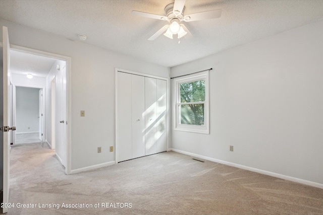 unfurnished bedroom with a textured ceiling, ceiling fan, a closet, and light colored carpet