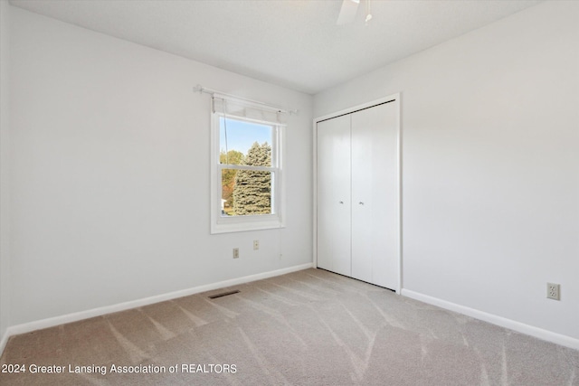 unfurnished bedroom featuring ceiling fan, light colored carpet, and a closet