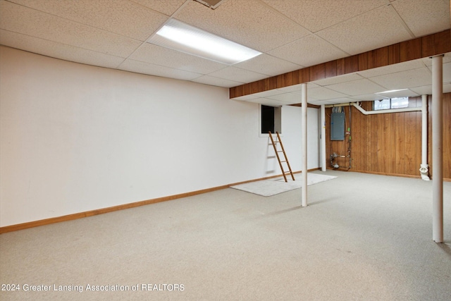 basement with electric panel, a paneled ceiling, wood walls, and carpet