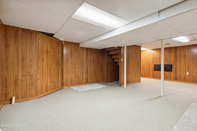 basement featuring carpet floors, a paneled ceiling, and wood walls